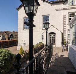An outdoor patio with black metal lamps and railing beside a white building with windows and a door at Gale Lodge Cottage in Ambleside