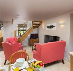 A living room with red armchairs a wooden staircase a dining table with food and drinks and a television at Barn Cottage in Bassenthwaite near Keswick