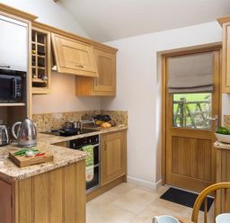 A kitchen with wooden cabinets toaster kettle microwave and a door at Barn Cottage in Bassenthwaite near Keswick
