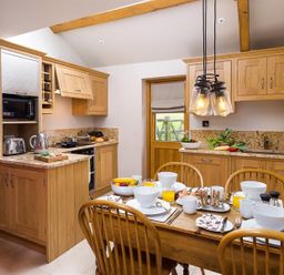 A kitchen with wooden cabinets dining table set with bowls cups and glasses at Barn Cottage in Bassenthwaite near Keswick