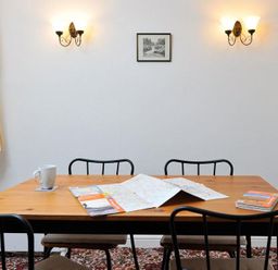 A wooden table with maps brochures and a mug with four black chairs and wall lights in a room at Mosslea in Bowness