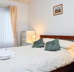 A bedroom with a double bed with white bedding and green pillows and bedside tables with lamps at Mosslea in Bowness