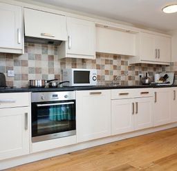 A kitchen with white cabinets a microwave stove oven kettle and cookware at Low Croft Cottage in Grasmere