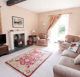 A living room with a TV on wooden stand a fireplace two armchairs a sofa and a red patterned rug at Robin Cottage in Troutbeck