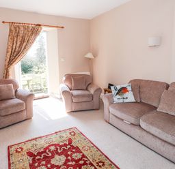 A living room with two armchairs and a sofa with cushions and a red patterned rug at Robin Cottage in Troutbeck