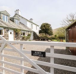 A white wooden gate with Robin Cottage sign in front of a stone cottage and courtyard at Robin Cottage in Troutbeck