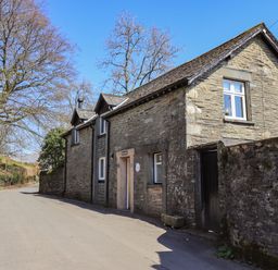 A stone house with white window frames beside a narrow road with trees in Troutbeck