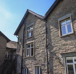 Exterior view of a stone building with multiple windows and a staircase at Boxwood Cottage in Troutbeck