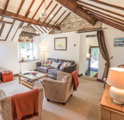 A living room with exposed wooden beams a leather sofa armchairs and a glass coffee table at Stablemans Cottage at Stepping Stones in Ambleside