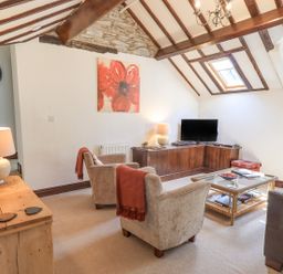 A living room with two armchairs a corner TV unit a coffee table and exposed wooden beams at Stablemans Cottage at Stepping Stones in Ambleside