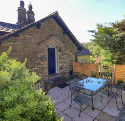 Outdoor patio with metal table and chairs beside stone cottage with blue door and greenery at Stablemans Cottage at Stepping Stones in Ambleside