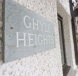 A close up of a sign that says Ghyll Heights on a rough white wall near a window and plants at Ghyll Heights in Ambleside