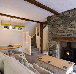 A living room with a stone fireplace a wooden coffee table a beige sofa a dining table and chairs and stairs at Acorn Cottage in Grasmere