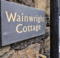 A close up of a stone wall with a sign reading Wainwright Cottage in Ambleside