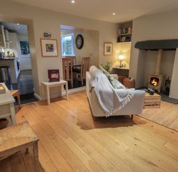 A living room with a sofa facing a wood burning stove a small table chairs and a dining area in the background at Wainwright Cottage in Ambleside