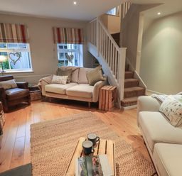 A living room with sofas a chair a wooden coffee table and stairs at Wainwright Cottage in Ambleside