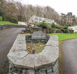 A stone sign reading Tannahiill beside a driveway with houses and trees in the background at Tanna Hill in Bowness