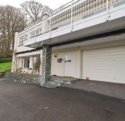 The exterior of a two-story house with a white front door a double garage door stone pillar and driveway at Tanna Hill in Bowness