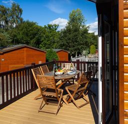 A wooden deck with a table and chairs set with food and drinks outside wooden cabins at Lancashire Rose in Ambleside