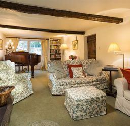 A living room with floral patterned sofas a piano a bookshelf and lamps at High Cleabarrow in Windermere