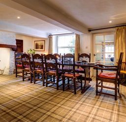 A dining room with a long wooden table and chairs near a window and fireplace at High Cleabarrow in Windermere