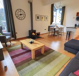A living room with a wood stove coffee table and dining table in an open plan kitchen at Idle Mill 2 in Ambleside