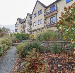 A gravel path leading to a three-story residential building with balconies and surrounding plants at Waterhead Retreat in Ambleside
