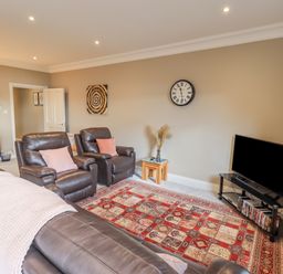 A living room with leather chairs a patterned rug a flat screen tv on a stand and a wall clock at Waterhead Retreat Ambleside