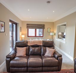 A living room with a dark leather sofa two cushions a window and a dining table at Waterhead Retreat in Ambleside