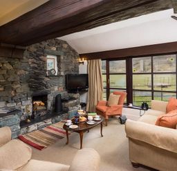 A living room with stone wall fireplace sofas armchair coffee table and large windows at Thirlmere Cottage in Grasmere