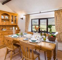 A dining room with a wooden table set with dishes and wine bottles near a window with floral curtains at Thirlmere Cottage in Grasmere