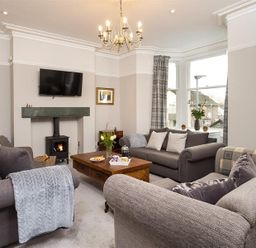A living room with three sofas a wooden coffee table a wall-mounted television and a wood-burning stove at Thirty Blencathra Street in Keswick