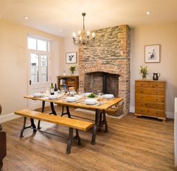 A dining room with a wooden table set for six near a stone fireplace at Thirty Blencathra Street in Keswick