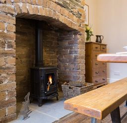 A stone fireplace with a wood burning stove a wooden bench a wooden dresser and a basket of logs at Thirty Blencathra Street in Keswick