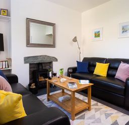 A living room with black sofas and colorful pillows around a wooden coffee table with drinks and snacks at Fell Cottage in Ambleside