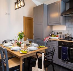 A kitchen with grey cabinets a wooden dining table set with plates glasses and a vase of flowers at Fell Cottage in Ambleside