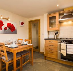 A kitchen with wooden cabinets a stove and a dining table set with dishes and glasses at Agathi in Keswick
