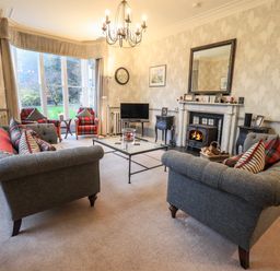 A living room with sofas a glass coffee table armchairs and a fireplace at Stepping Stones House in Ambleside