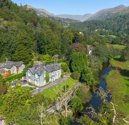 A countryside stone house near a river surrounded by trees and hills at Stepping Stones House in Ambleside