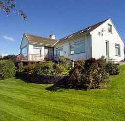 White house with sloped roof surrounded by green grass and bushes under a blue sky at Primrose Mount in Bowness