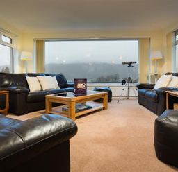 A living room with black leather sofas wooden tables a coffee table and a telescope at Primrose Mount in Bowness