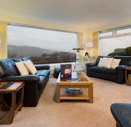 A living room with leather sofas coffee table telescope and large windows at Primrose Mount in Bowness