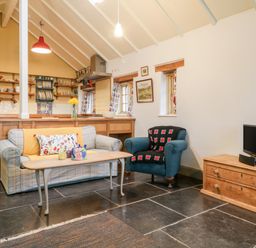 A living room with a sofa and armchair a coffee table and a television on a wooden cabinet at Old Cary Cottage Henley near Langport