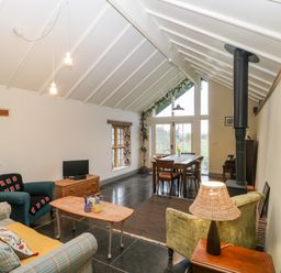 A room with a seating area including chairs and sofa a dining table near large windows and a wood stove at Old Cary Cottage Henley near Langport