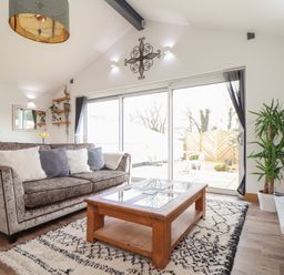 A living room with a sofa, coffee table, potted plant, wall-mounted TV, and glass sliding doors at Chycoose Hicks Mill near Perranarworthal