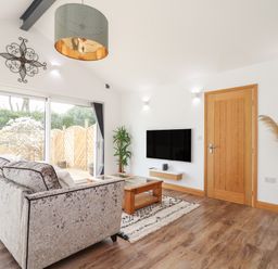 A living room with a sofa coffee table wall mounted tv and sliding glass doors at Chycoose in Hicks Mill near Perranarworthal