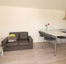 A small living area with a dark sofa and pillows next to a kitchen counter with three chairs and flowers at Coolnaharragill Lower Annexe in Glenbeigh County Kerry