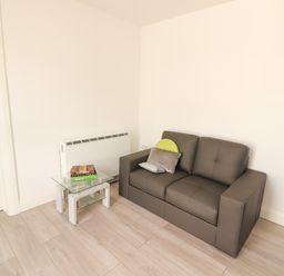 A small living room with a grey sofa and a glass side table with books at Coolnaharragill Lower Annexe in Glenbeigh County Kerry