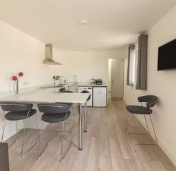 A kitchen with a countertop and bar stools a washing machine a refrigerator a tv mounted on the wall at Coolnaharragill Lower Annexe in Glenbeigh County Kerry