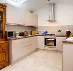 A kitchen with beige cabinets a wooden cupboard a microwave an oven a gas stove and kitchen utensils at Fern Cottage in Ambleside